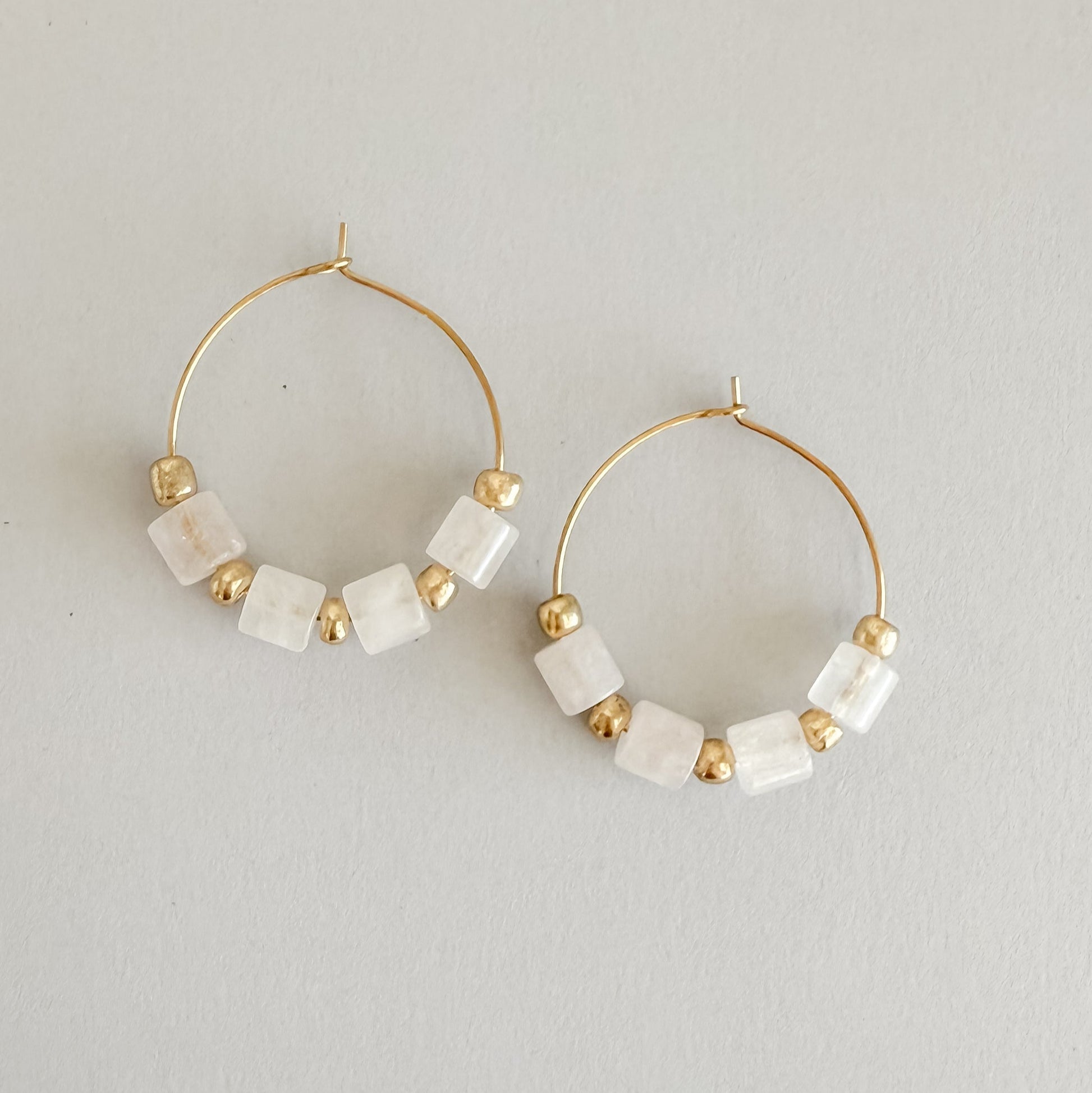 Gold hoop earrings with white beads on a light gray background