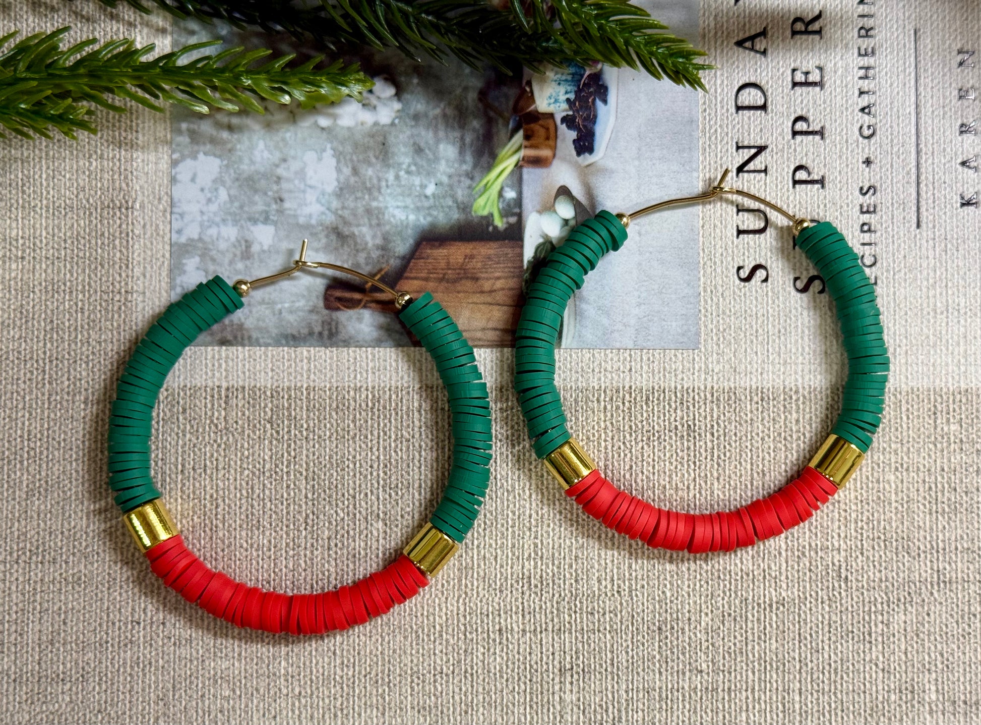 Green and red hoop earrings with gold accents on a textured surface.