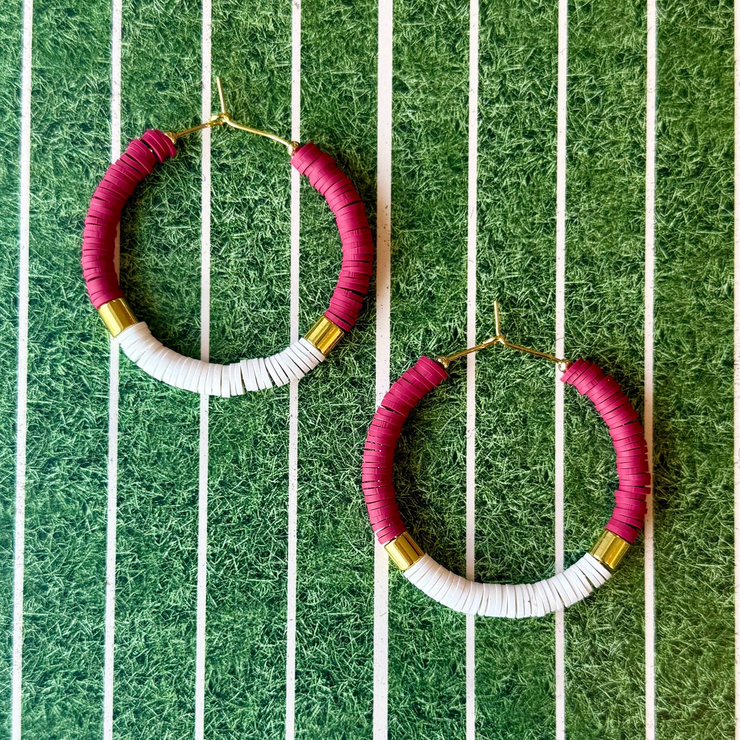 Hoop earrings with maroon, white, and gold accents on a green and white striped background