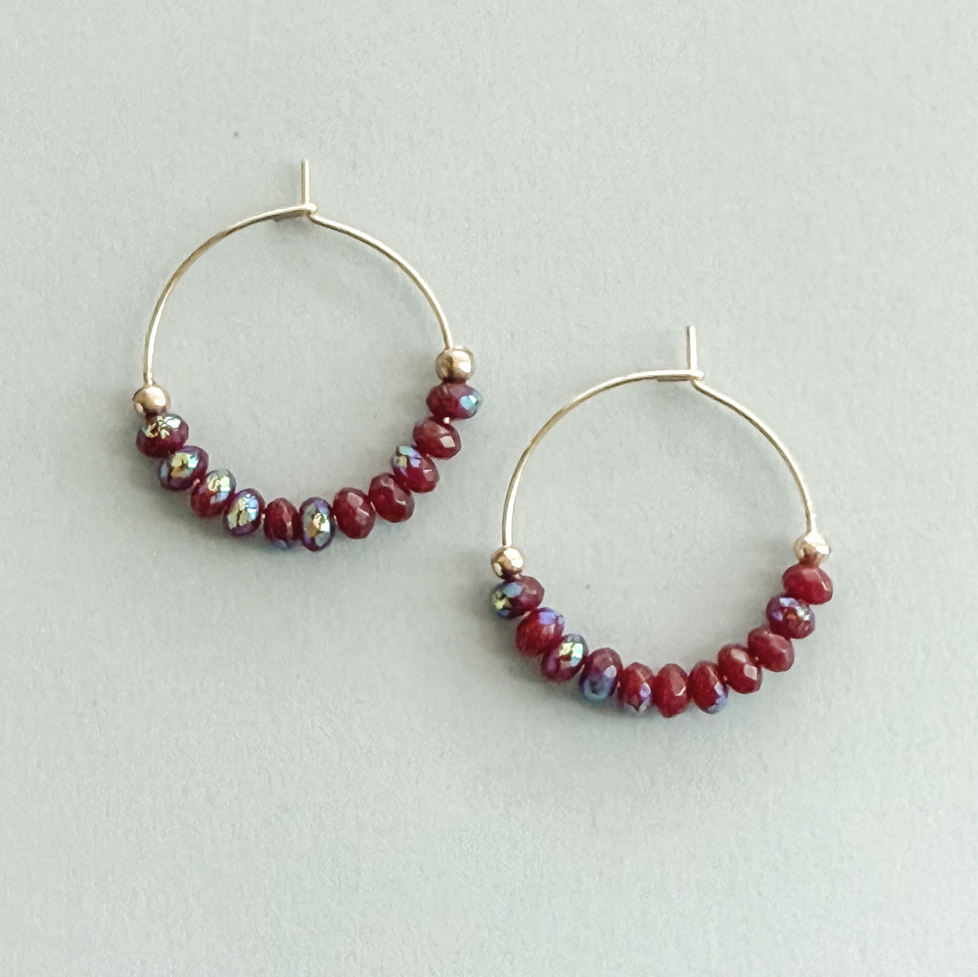 Hoop earrings with red bead accents on a light gray background