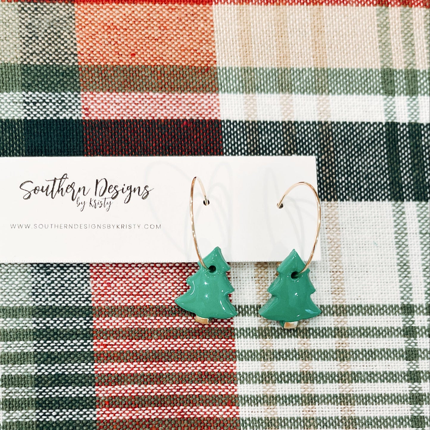 A pair of green Christmas tree dangle ornaments with a plaid background and 'Southern Designs by Kristy' tag on the fabric.