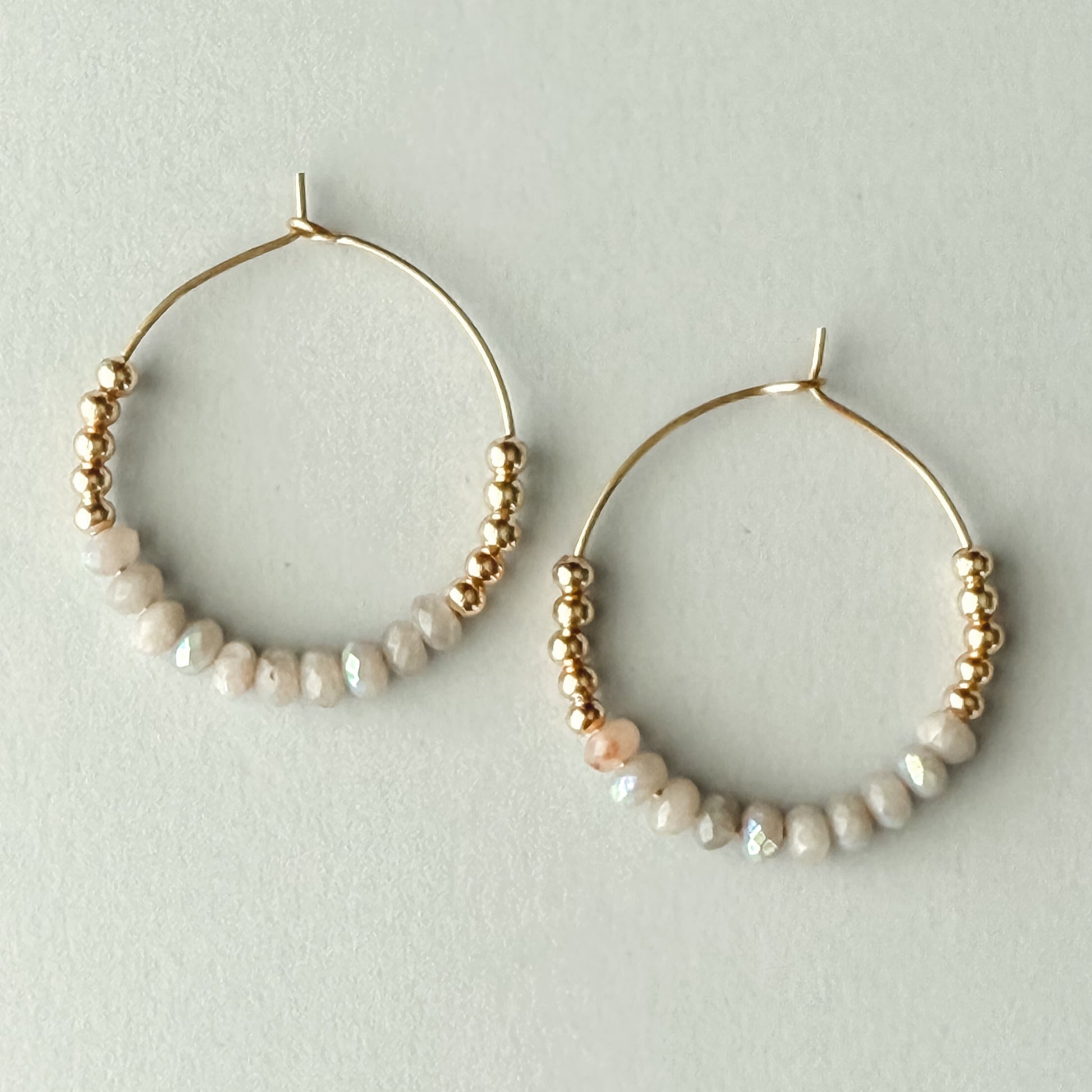 Gold hoop earrings with pearl beads on a light gray background