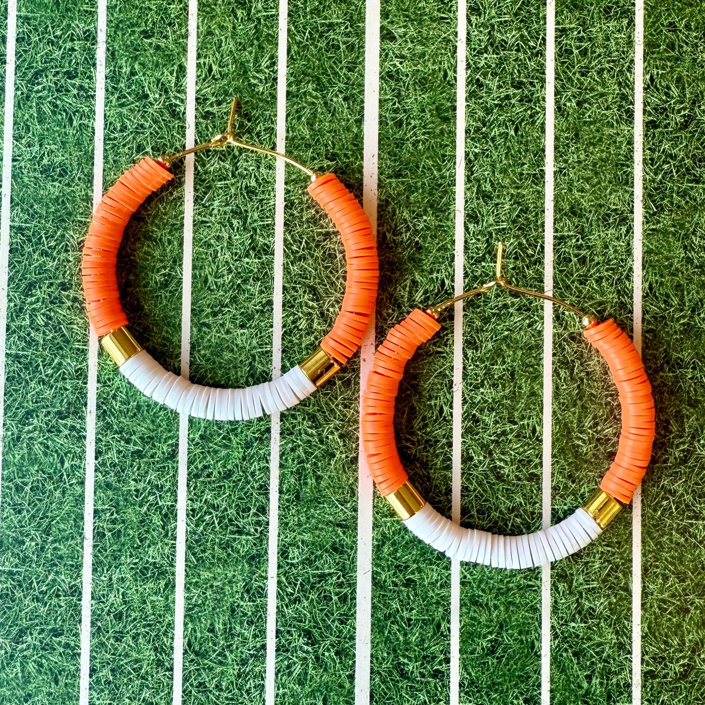 Hoop earrings with orange, white, and gold beads on a striped green and white background