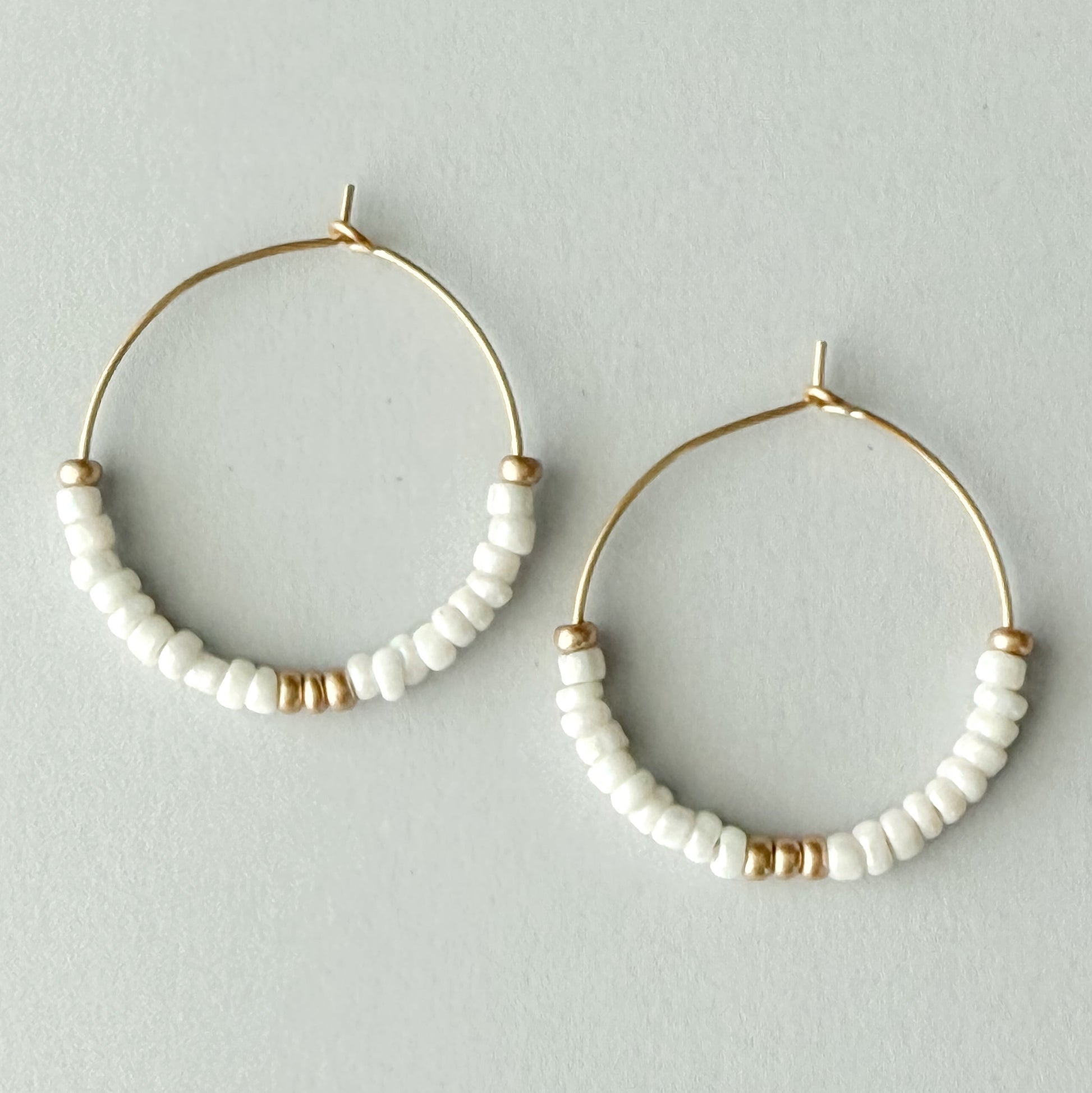 Pair of gold hoop earrings with white beaded accents on a light gray background