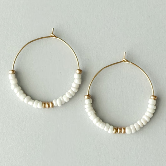 Pair of gold hoop earrings with white beaded accents on a light gray background