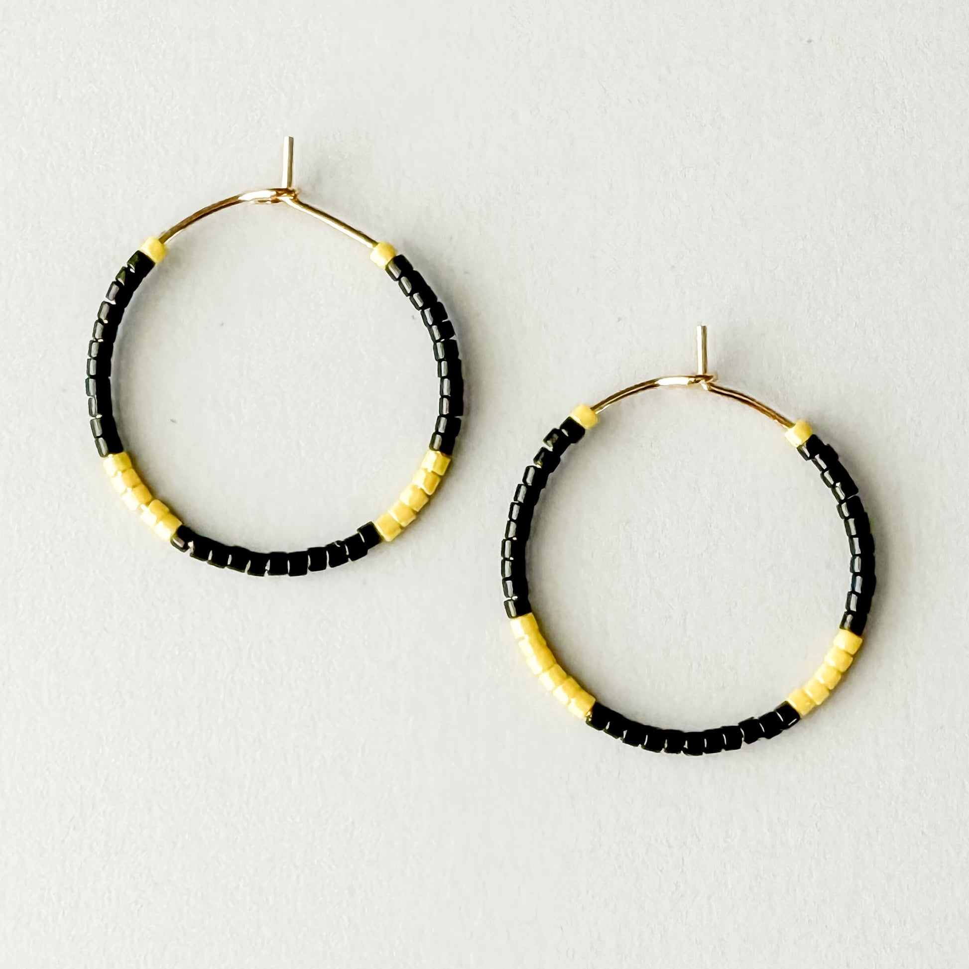 Hoop earrings with black and yellow beads on a light gray background