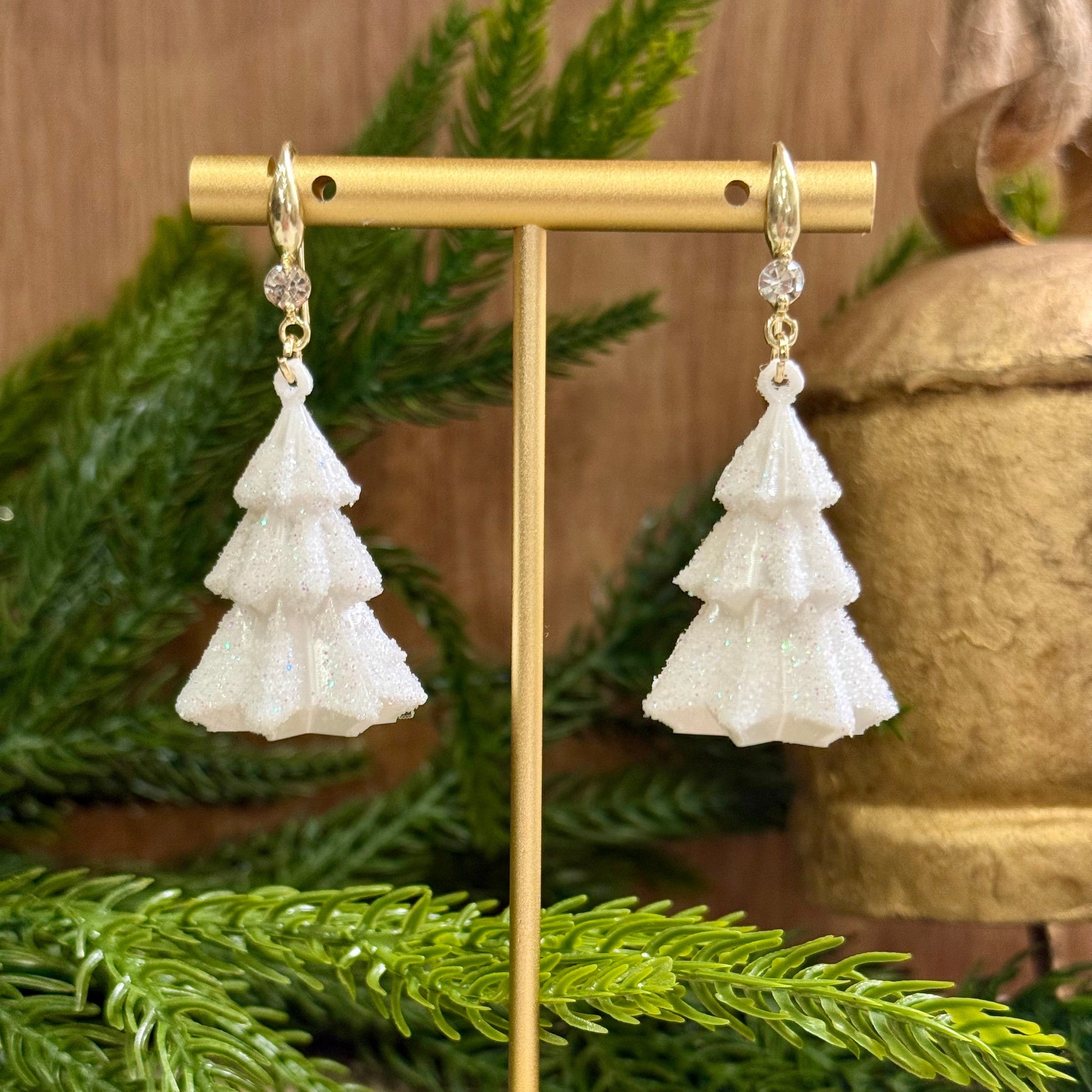 White snow tiered earrings on a gold stand with green foliage in the background