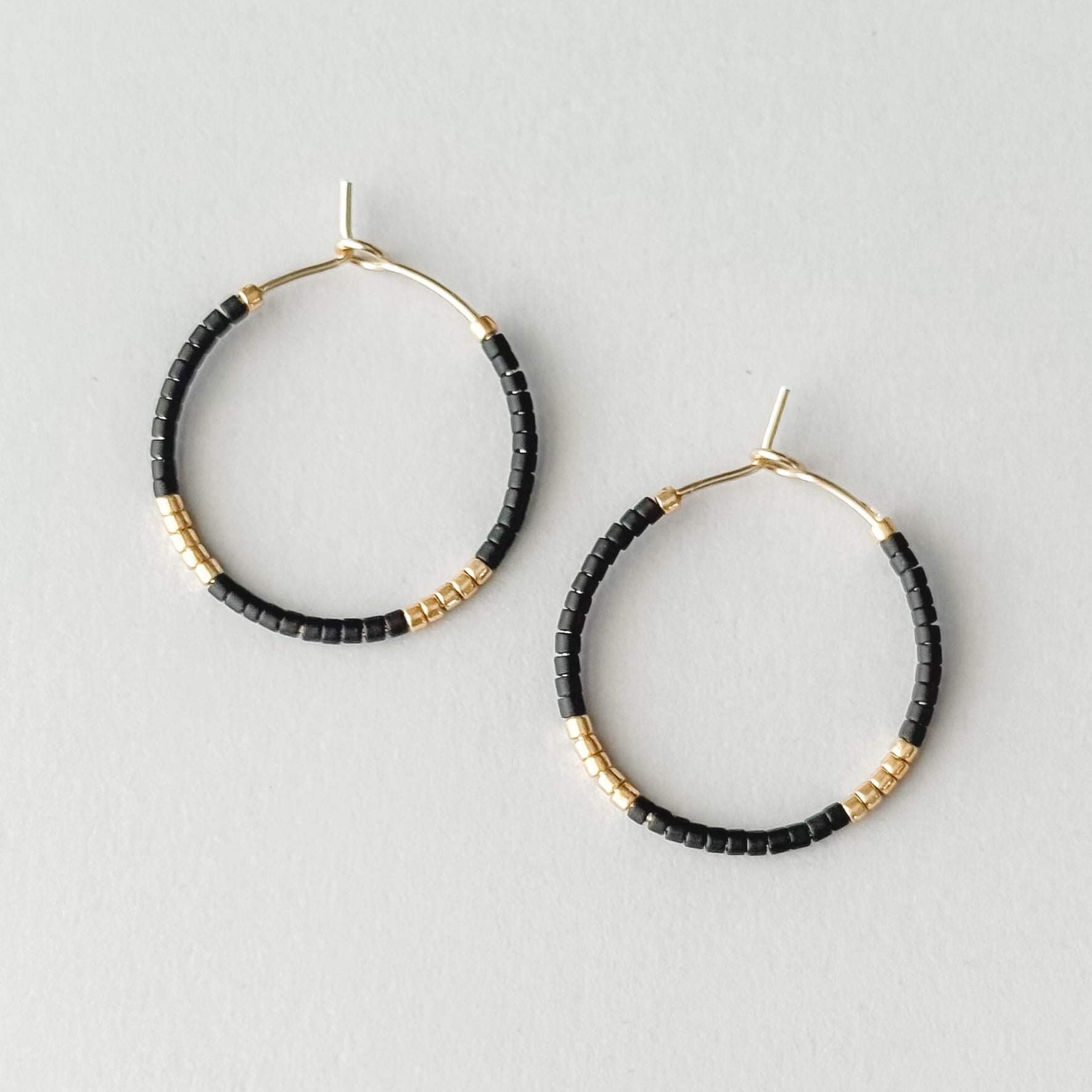Black beaded hoop earrings with gold accents on a light gray background