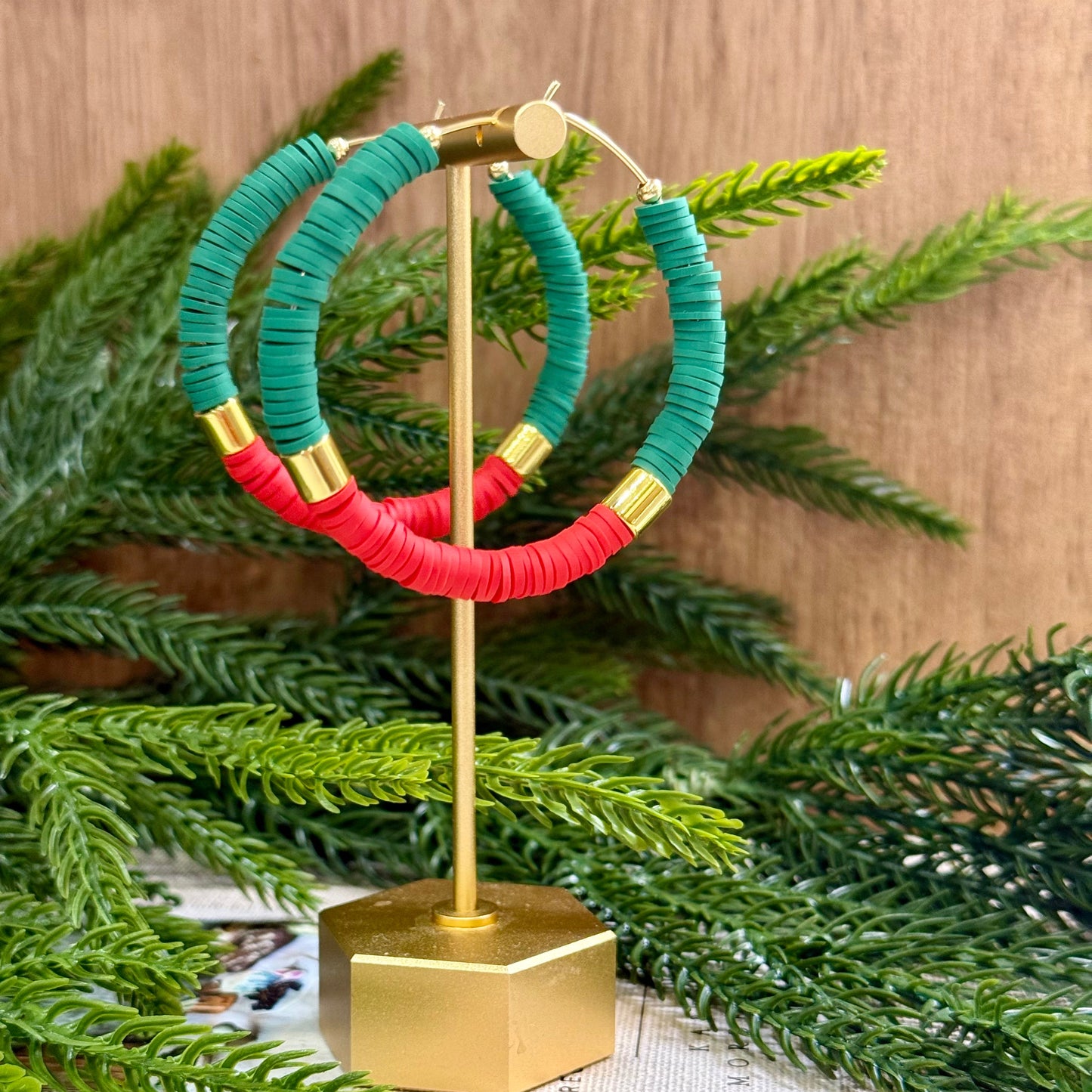 Green and red hoop earrings on a gold stand with greenery in the background