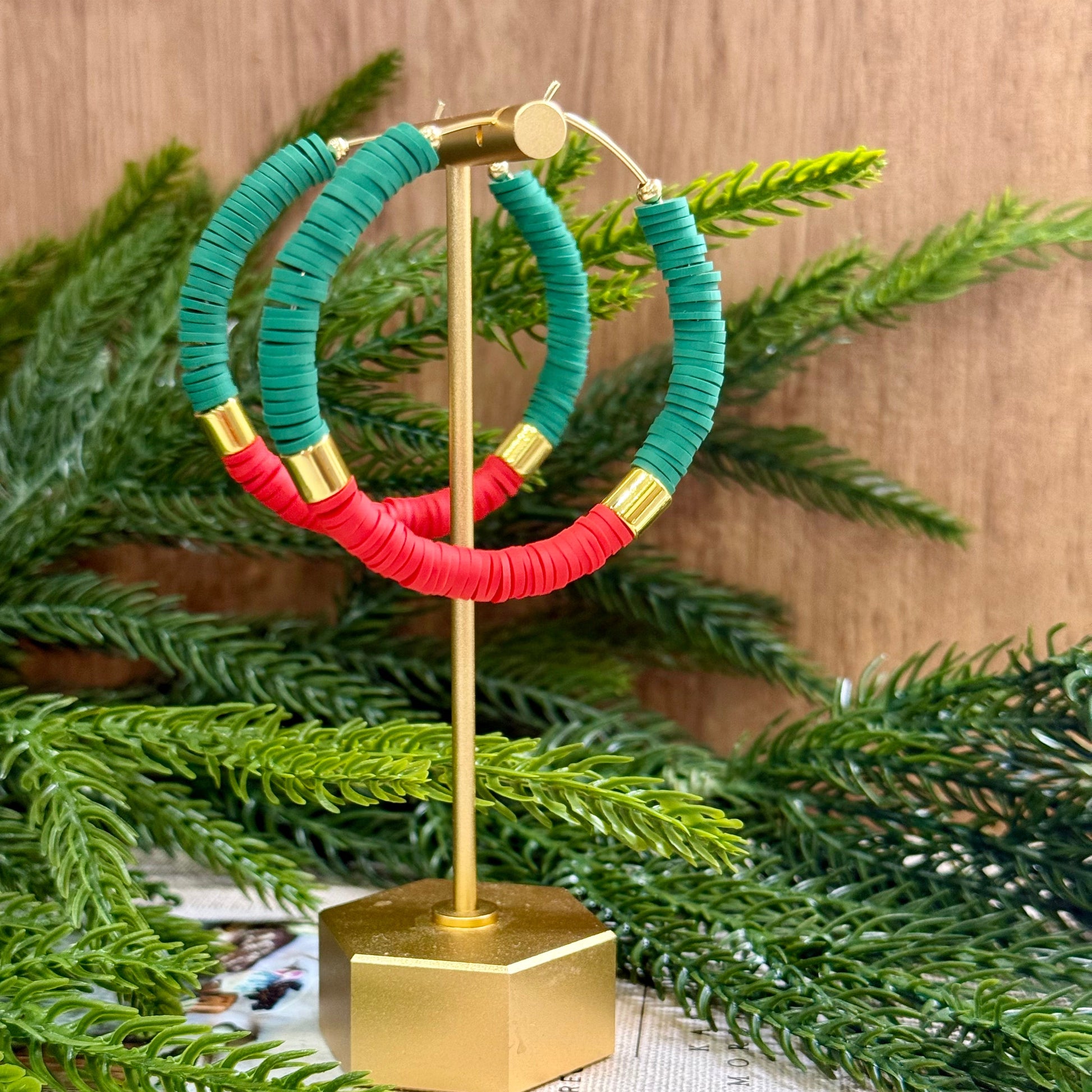 Green and red hoop earrings on a gold stand with greenery in the background
