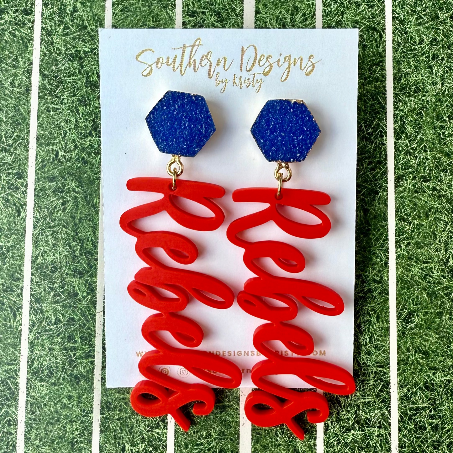 Red 'Rebels' earrings with blue hexagonal stones on a card labeled 'Southern Designs by Kristy' against a green and white striped background.