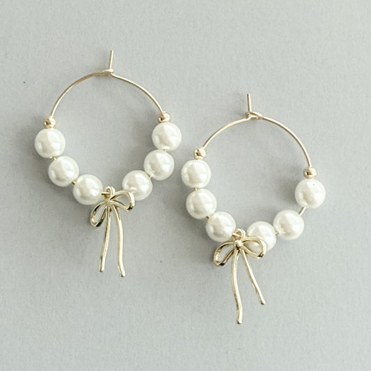 Pearl hoop earrings with gold bows on a light gray background