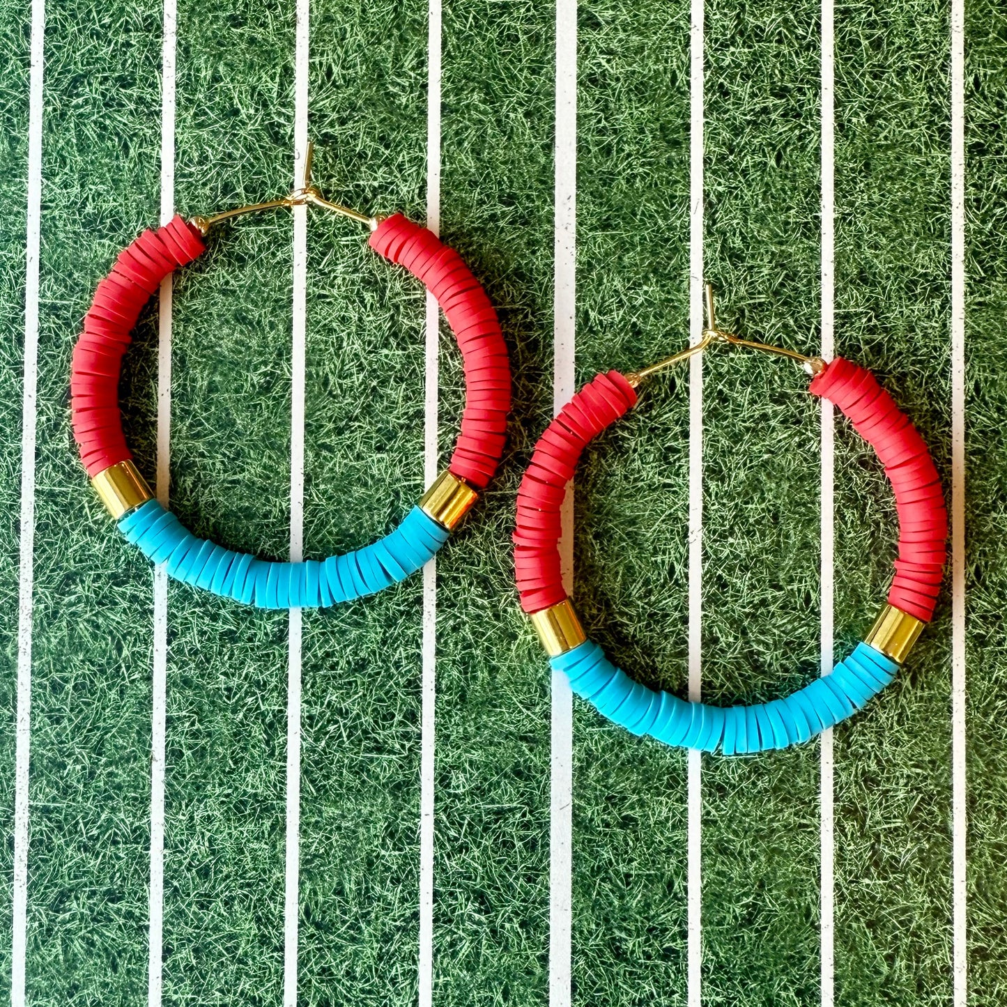 Colorful hoop earrings with red, blue, and gold accents on a green and white striped background.