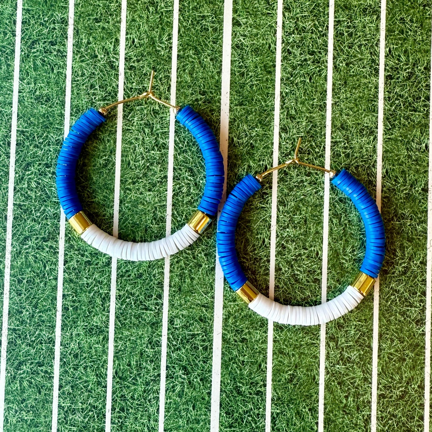 Blue and white hoop earrings with gold accents on a green and white striped background