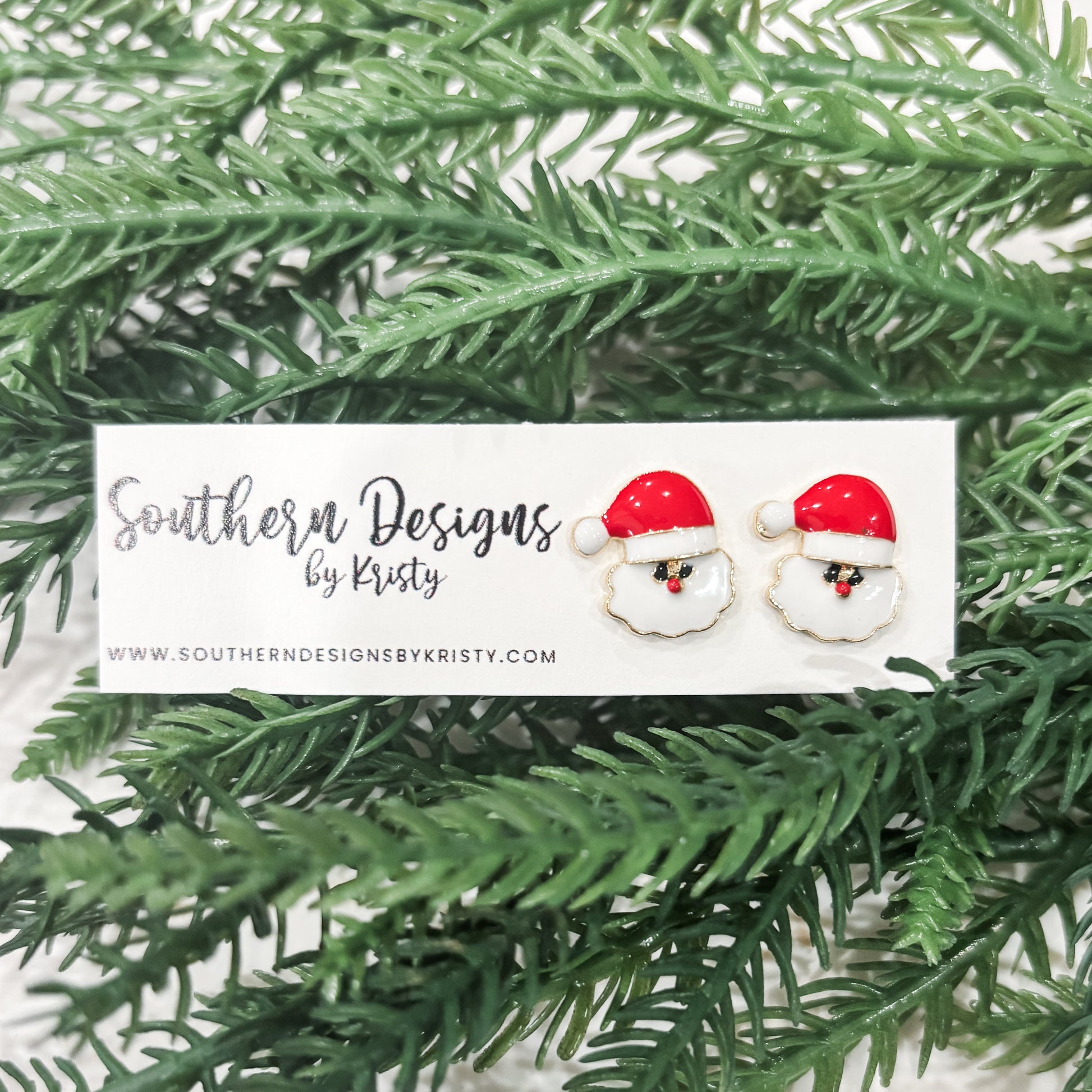 This image displays a pair of charming "Santa Studs" earrings, perfect for adding a festive touch to any outfit. The earrings feature a playful design with a red and white Santa hat motif, set against a soft, green backdrop that highlights their holiday spirit.