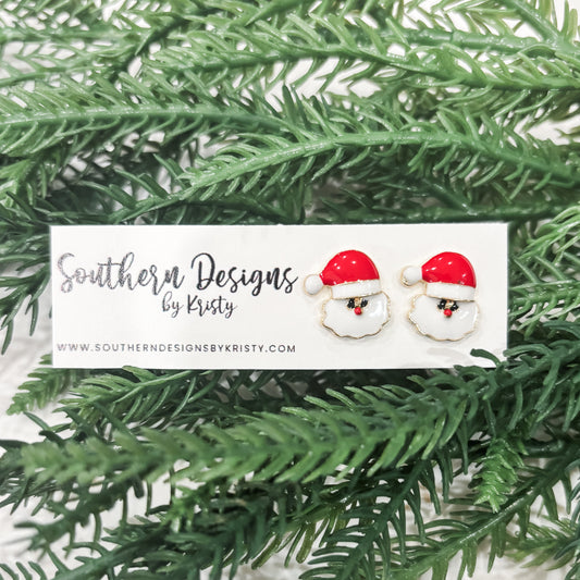 This image displays a pair of charming "Santa Studs" earrings, perfect for adding a festive touch to any outfit. The earrings feature a playful design with a red and white Santa hat motif, set against a soft, green backdrop that highlights their holiday spirit.