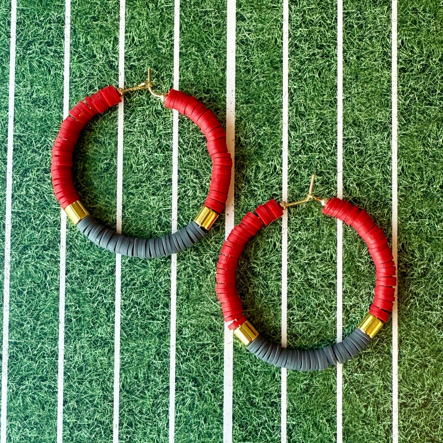 Pair of hoop earrings with crimson, gray, and gold accents on a grassy background.