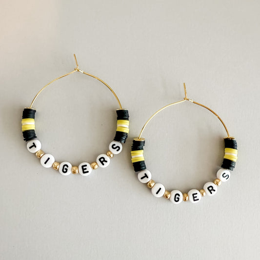 Hoop earrings with 'TIGERS' beads on a light gray background