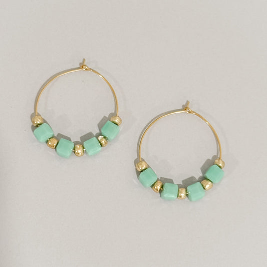 Gold hoop earrings with turquoise beads on a light gray background